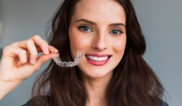 Smiling woman holding clear aligners for teeth straightening treatment