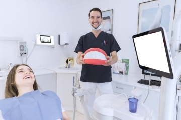 happy male dentist holding teeth model