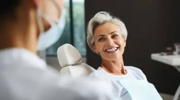 Smiling mature woman sitting in a dental chair during a routine dental checkup at a modern dental clinic.