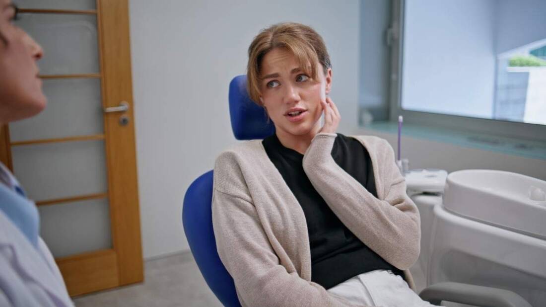 Adult patient holding her jaw while speaking with a dentist during a family dental consultation