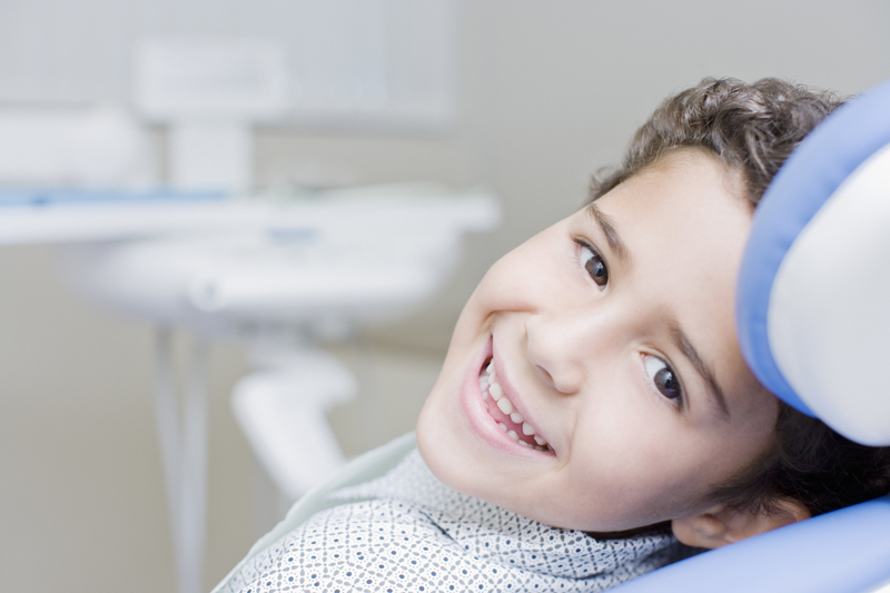 Boy smiling and sitting in a family dentist's chair for regular teeth cleaning services
