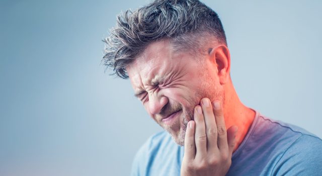 Man in pain with hand on cheek.